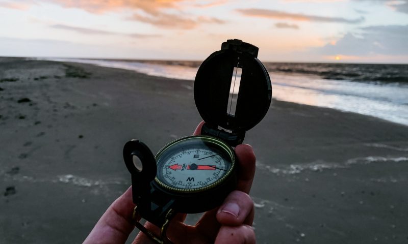 hand holding a compass on a beach
