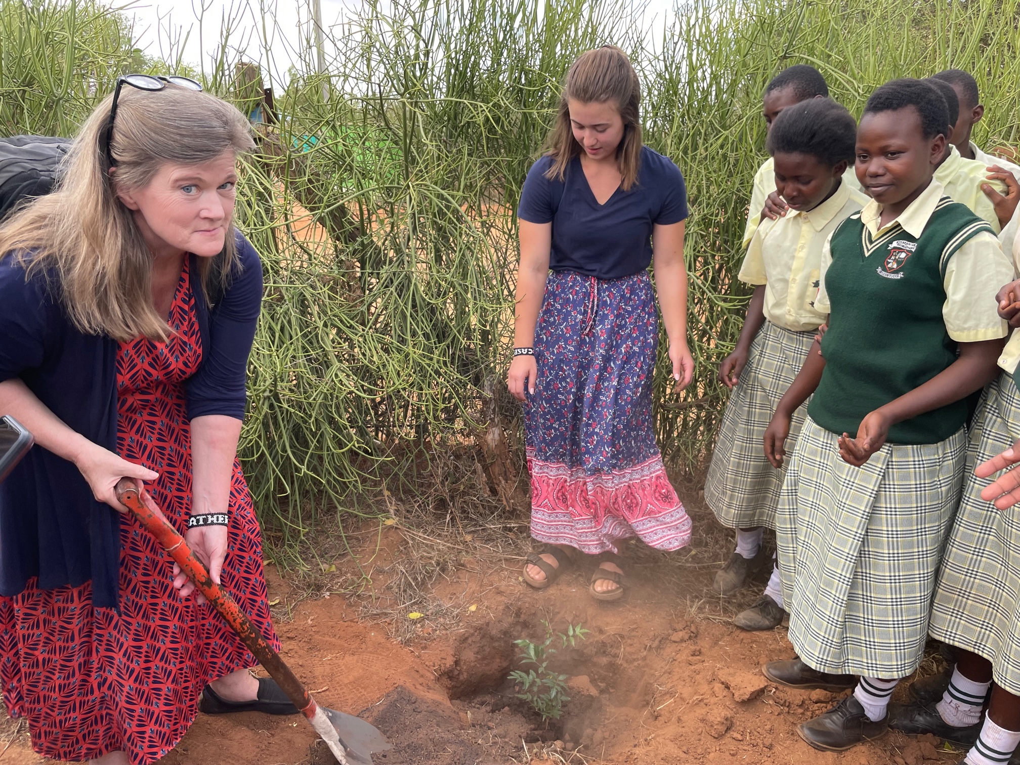 Dr. Heather E. Eves (far left) plants a tree at a high school in Kenya with former student Rachael Mwikali (not pictured), who runs a non-profit called Kibwezi WellWishers (Centre for Sustainability) which focuses on education, health, and environment. Eves’ daughter, Casey, (center) accompanied her on the trip. Photo courtesy of Dr. Heather E. Eves.