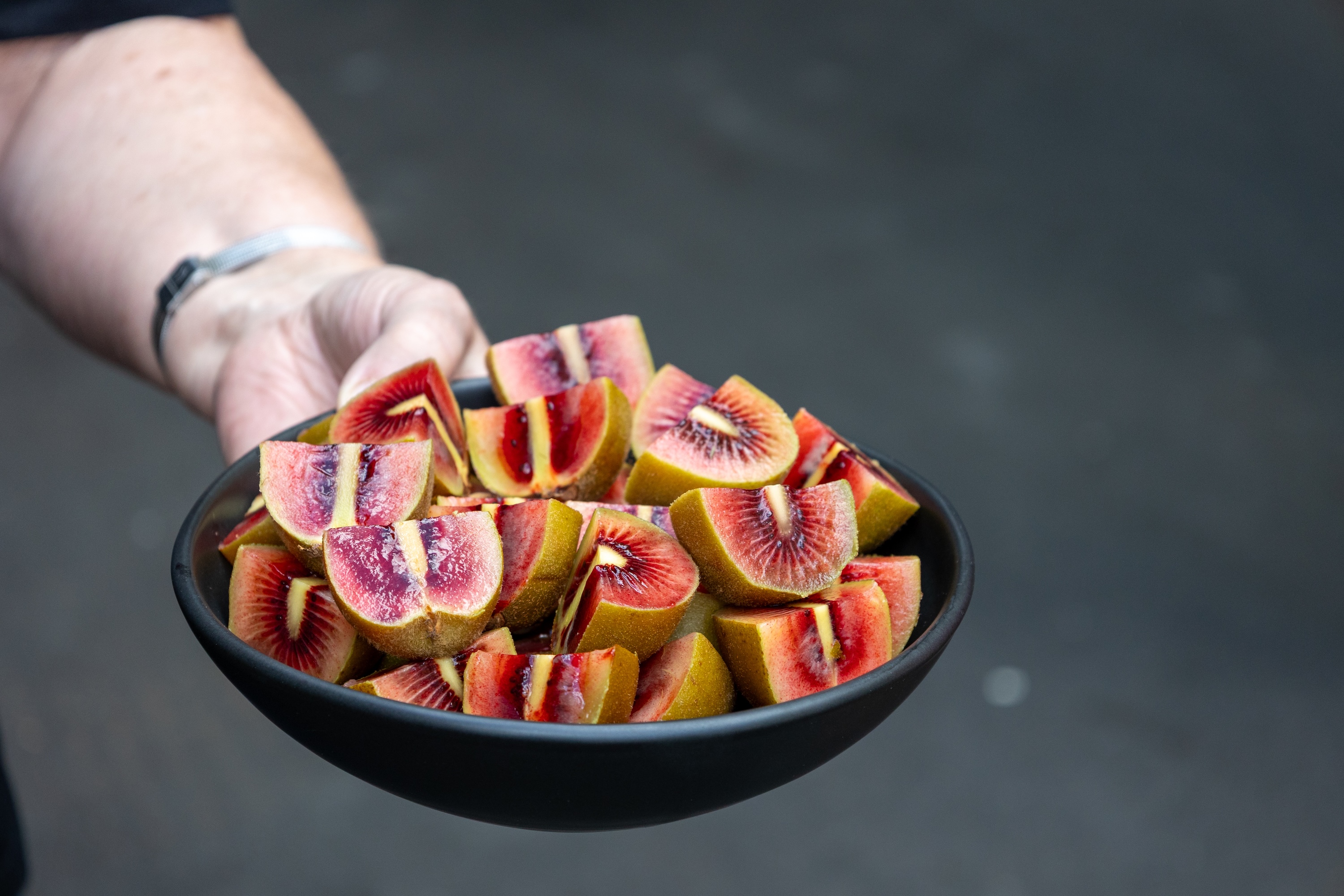 woman holds out a bowl of kiwi