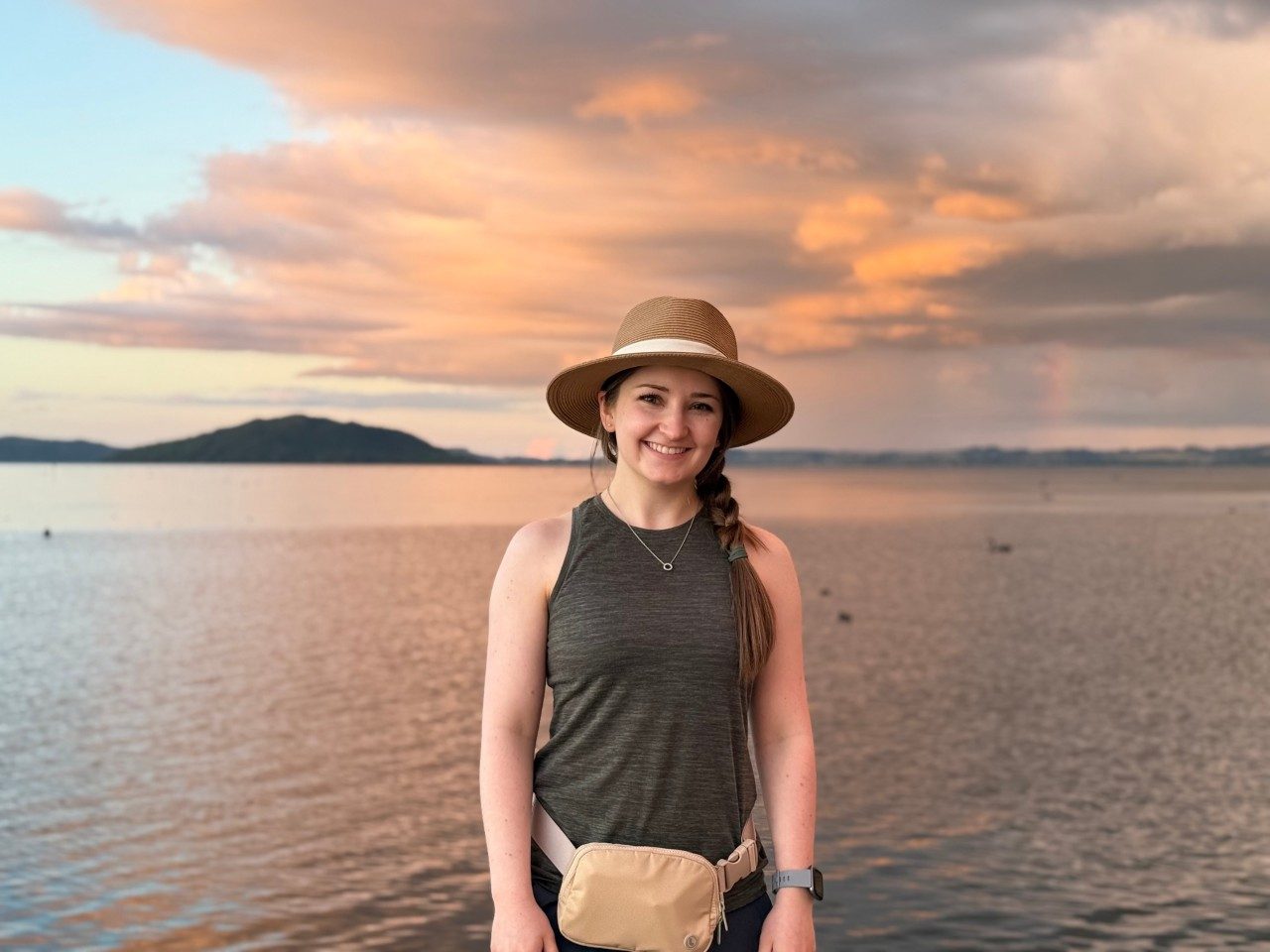woman with tan hat and sleeveless shirt stand in front of a sunset